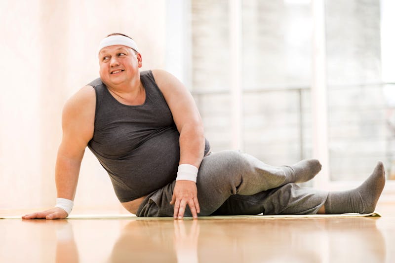 Smiling fat man stretching on the floor.