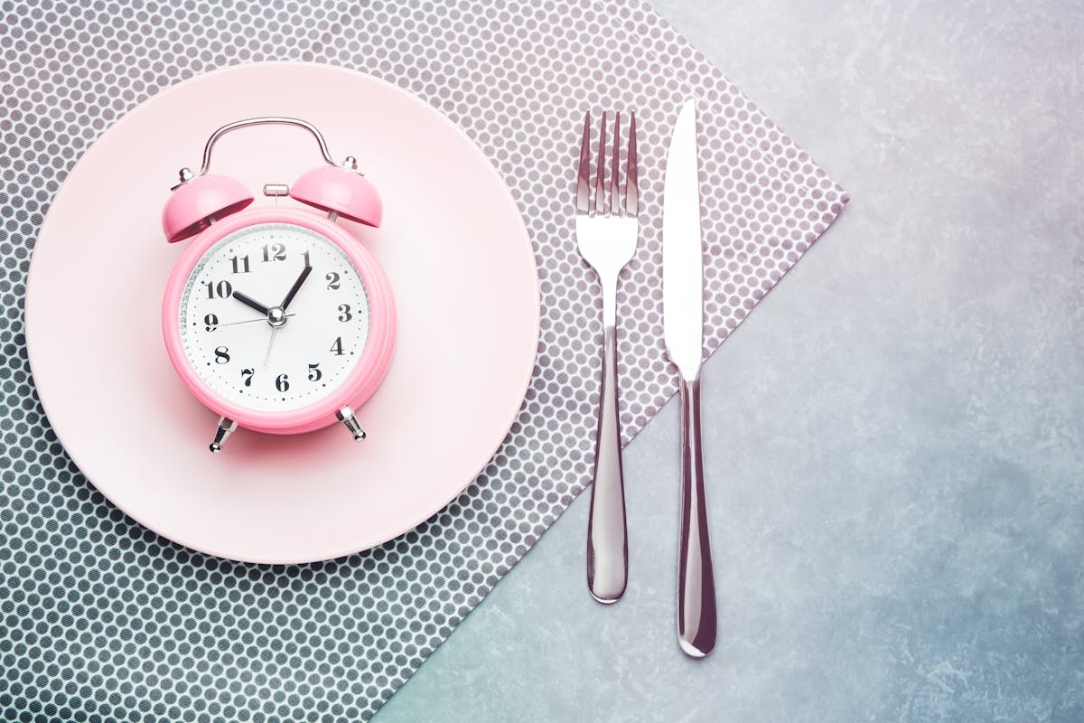 Alarm clock and plate with cutlery. Concept of intermittent fasting, lunchtime, diet and weight loss