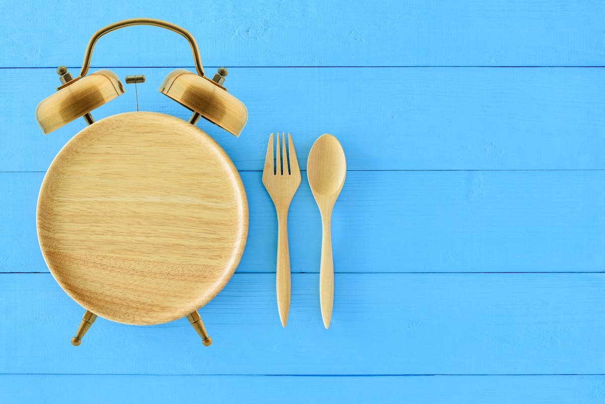 Intermittent fasting, diet and weight loss concept : Clock shaped wood dish, spoon and fork. Eco-friendly plate / kitchen utensil as alarm clock with ringing bell, depict alert or reminder time to eat