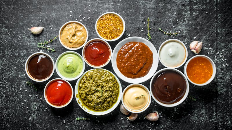 Pesto sauce, guacomole, ketchup, mustard, barbecue sauce in bowls.