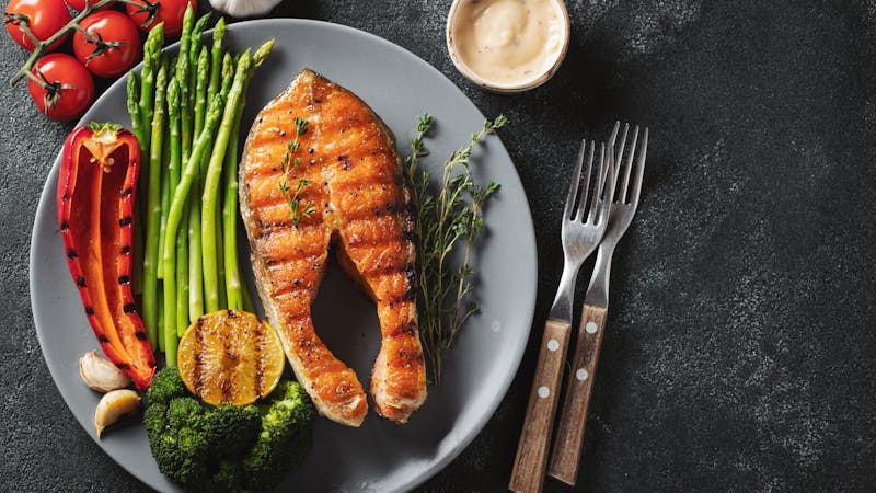 Tasty and healthy salmon steak with asparagus, broccoli and red pepper on a gray plate. Diet food on a dark background with copy space. Top view. Flat lay
