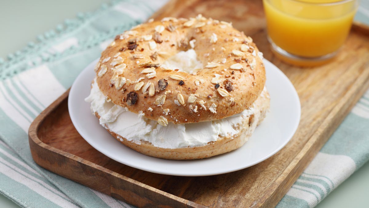 Breakfast with soft cheese bagel sandwich and a cup of orange juice