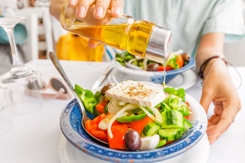 Woman pouring delicious Olive oil into greek salad in restaurant. Healthy food and vegetarian concept