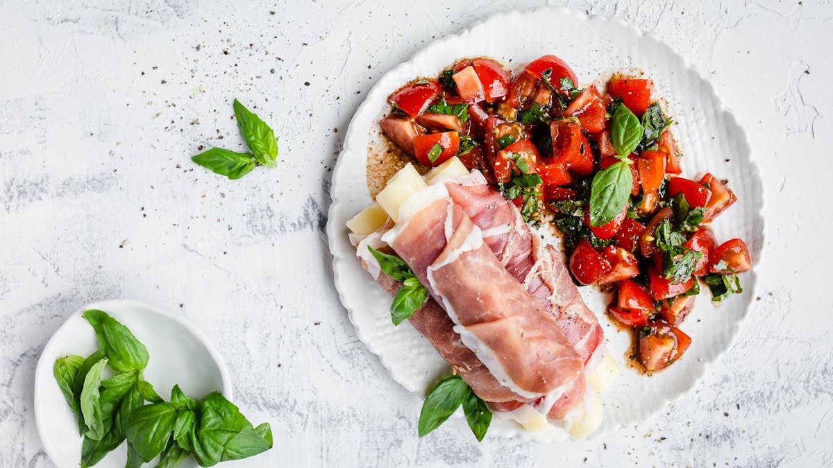 Palitos de mozzarella envueltos en prosciutto con ensalada de tomate y albahaca