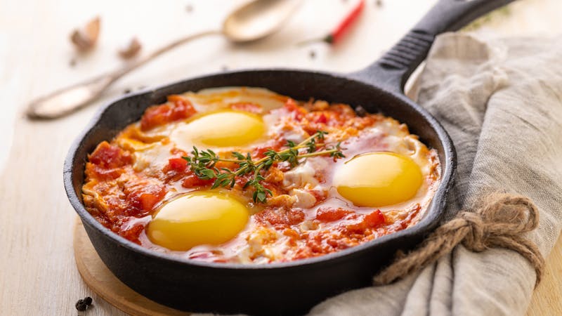 Shakshuka. Fried eggs with tomatoes and sweet pepper and herbs in a serving cast-iron frying pan.