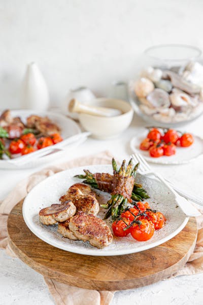 Chuletas de cerdo con judías verdes enrolladas en bacon y tomates asados