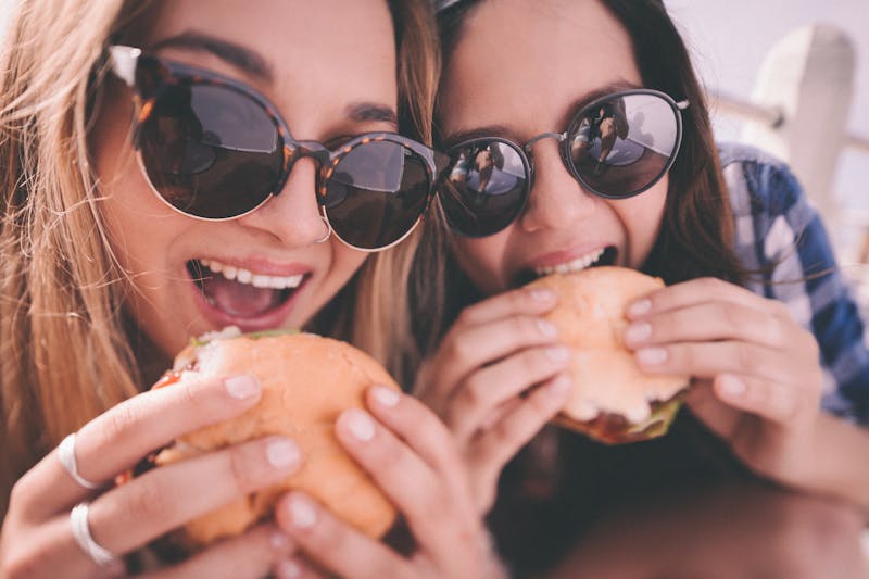Retro style shot of teenage girl best friends eating burgers
