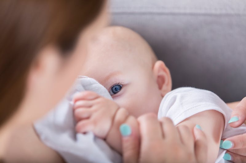 Adorable blue eyed baby looks at mom while breastfeeding
