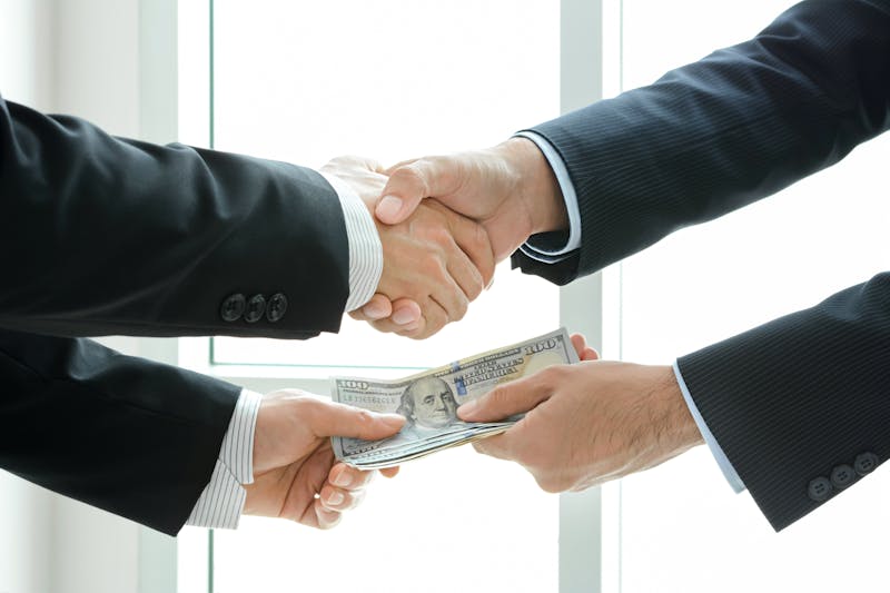 Businessmen making handshake while passing money