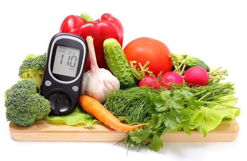 Glucometer and fresh vegetables on wooden cutting board