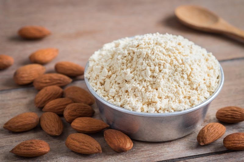 Almond flour in bowl and almonds on wooden table
