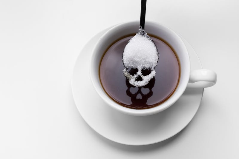 unhealthy white sugar concept. Scull spoon with sugar and cup of black coffee