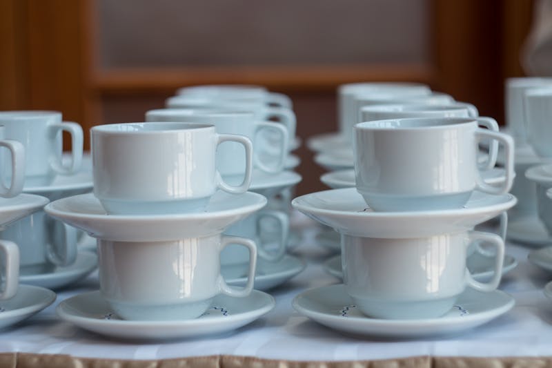 White cups for tea piled on table with plates for coffee-break. Catering concept.