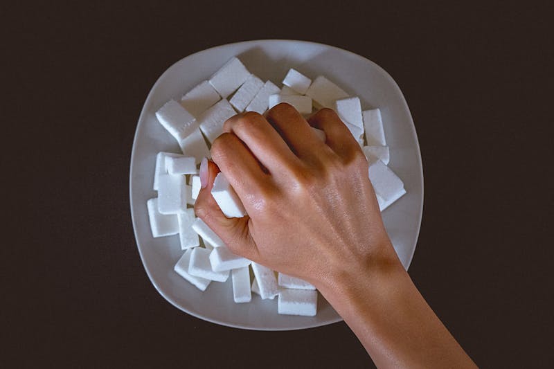 Female hand grabbing a bunch of sugar cubes from the plate on the table