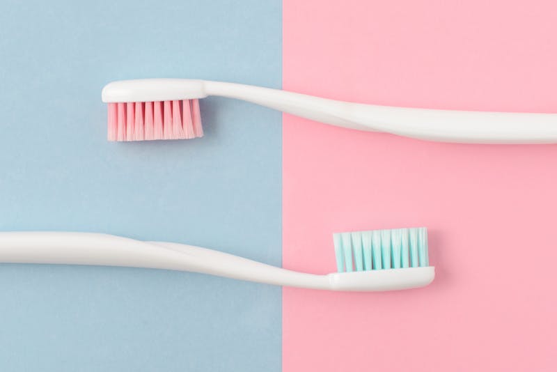 Close up of two plastic white toothbrushes with pink and blue bristle on pink and blue background. Free copy space.