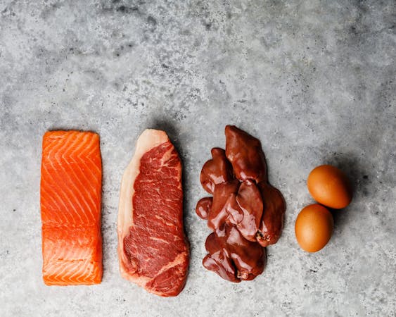 Raw food selection for Ketogenic diet Egg, Chicken Liver, Beef meat Steak and Salmon fish Steak on gray concrete background copy space