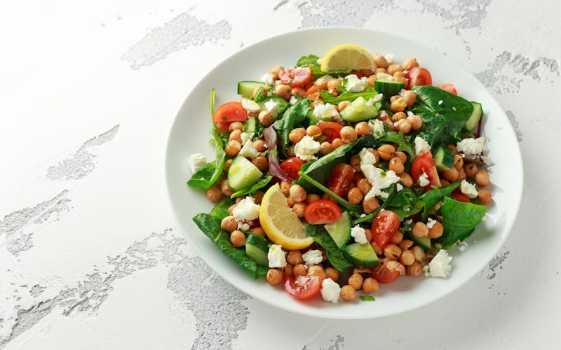 Chickpeas Salad with cucumber, tomatoes, feta cheese and green mix in a white plate. healthy food.