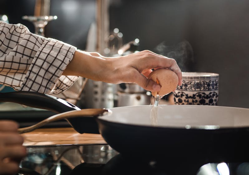 Close up of unrecognizable woman cracking an egg before preparing it in a frying pan.