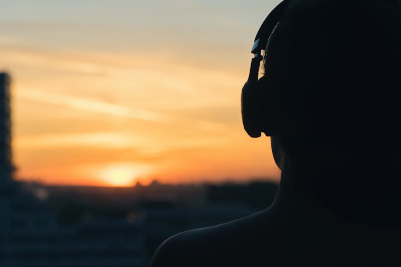 Girl in headphones listening to music in the city at sunset