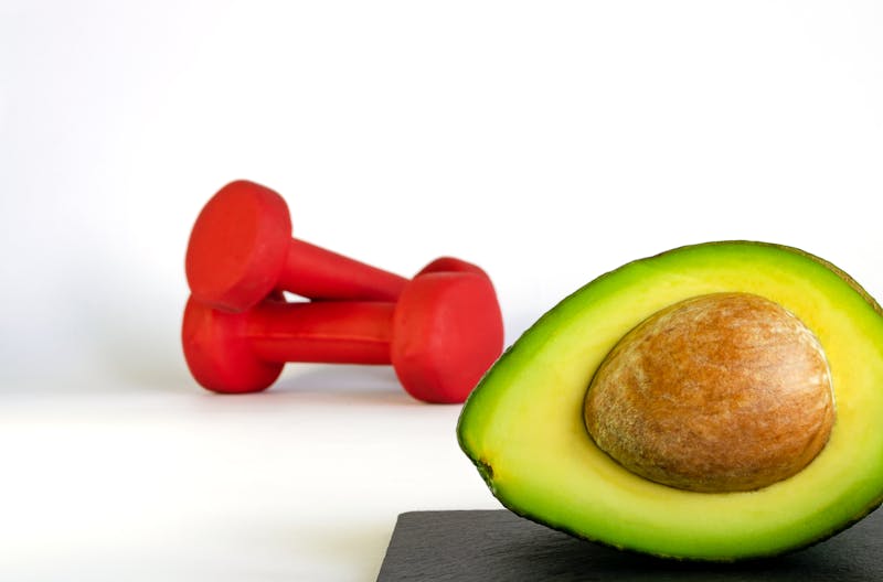 Fresh avocado with unfocused red dumbbells on background. Concept of healthy eating and sports.