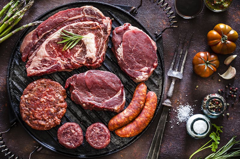 Various cuts of raw meat shot from above on a cast iron grill