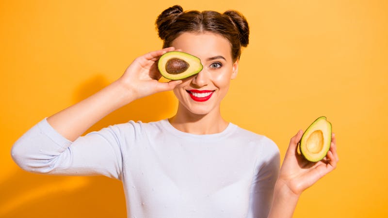 Close up photo beautiful she her lady pretty hairdo hold slices avocado hide eye used amazing salon mask oil extract procedure wearing casual white pullover clothes isolated yellow background