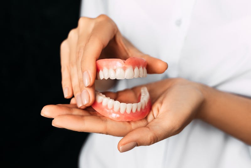 The dentist is holding dentures in his hands. Dental prosthesis in the hands of the doctor close-up. Front view of complete denture. Dentistry conceptual photo. Prosthetic dentistry. False teeth