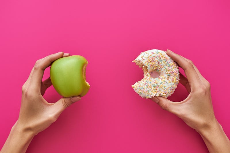 Dieting or good health concept. Young woman trying to choose between apple and donut