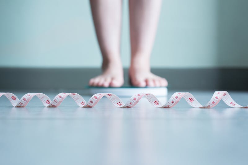 Blured of woman foot standing on weigh scales with tape measure in foreground