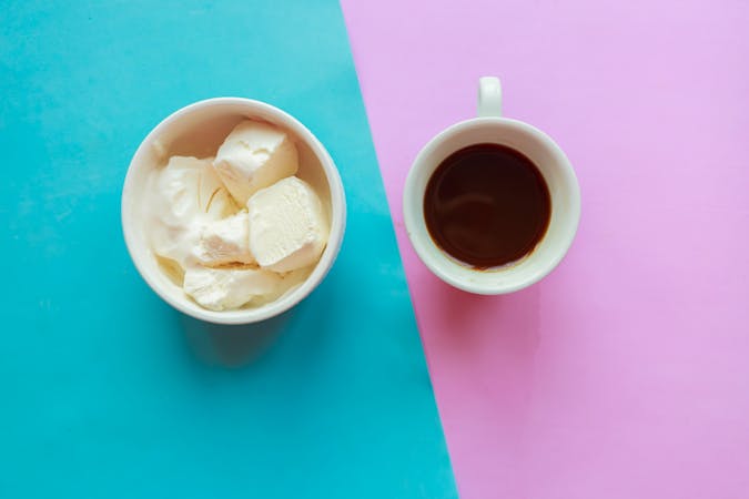 Vanilla ice cream bowl and coffee cup on pink and blue background, top view