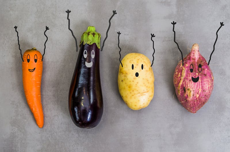 Great concept of healthy eating, vegetables with happy faces with arms up, potato, sweet potato, carrot, eggplant. Gray background, polished concrete.