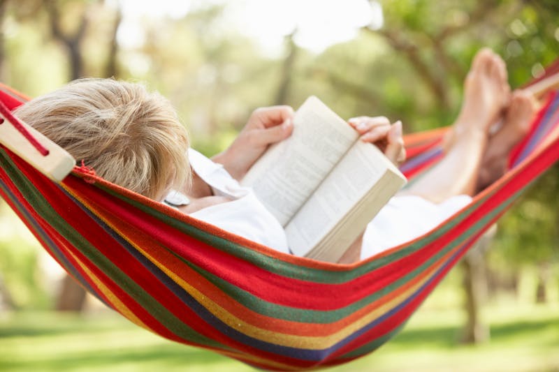 Senior Woman Relaxing In Hammock With Book