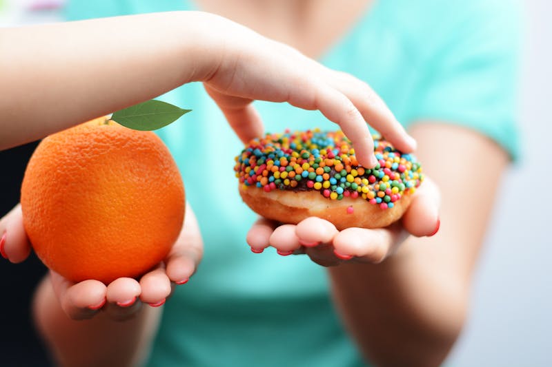Child obesity concept with little girl hand choosing a sweet and unhealthy doughnut instead of a fruit