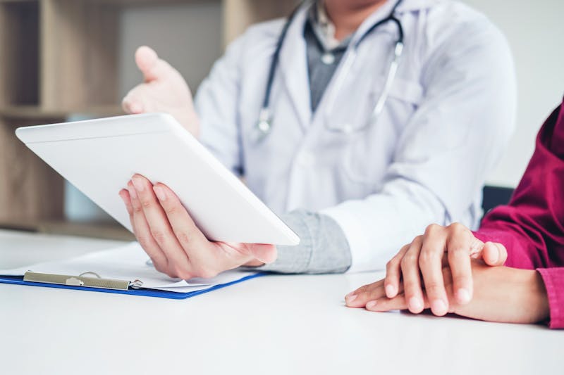 Doctor consulting with patient presenting results on digital tablet tablet sitting at table