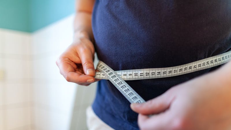 man measures her abdomen with a measuring tape