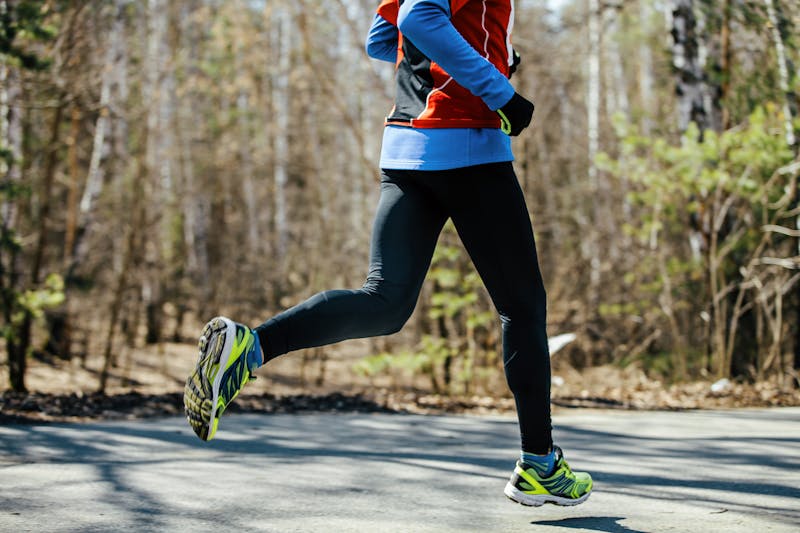 feet athletic male runner runs asphalt road in spring park