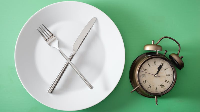 concept of intermittent fasting, ketogenic diet, weight loss. fork and knife crossed on a plate and alarmclock