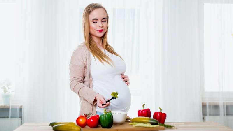 Smiling pregnant woman eating vegetables salad for health