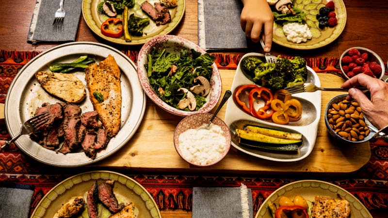 A ketogenic meal laid out on a dining table with the hands of people serving themselves