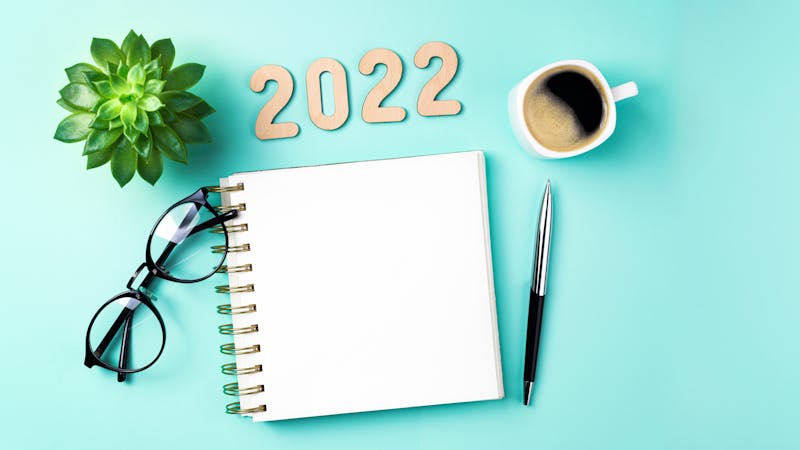 New year 2022 goals on desk. 2022 resolutions with open notebook, coffee cup, eyeglasses, plant succulent on green background. Goals, resolutions, plan, strategy, idea concept. New Year 2022