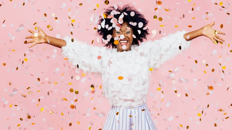 Happy young woman celebrating with arms out and lots of falling confetti