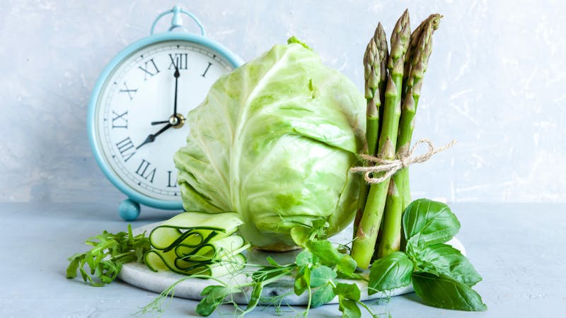 Alarm clock, Asparagus, microgreens, cucumber and cabbage – fresh green vegetables. Ketogenic diet, intermittent fasting, weight loss