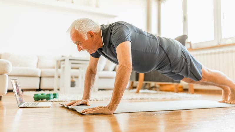 Active senior man home exercising with online coach