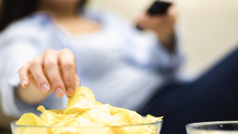 Unrecognizable woman is eating potato chips. Close up huge deep plate, full of potato chips.