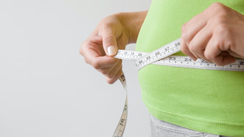 Fat overweight woman measuring her waist. Plus size. New start for healthy lifestyle, body slimming and weight loss. Care about body. Copy space. Empty place for text on gray background.