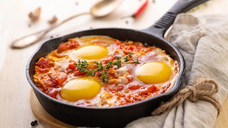 Shakshuka. Fried eggs with tomatoes and sweet pepper and herbs in a serving cast-iron frying pan.