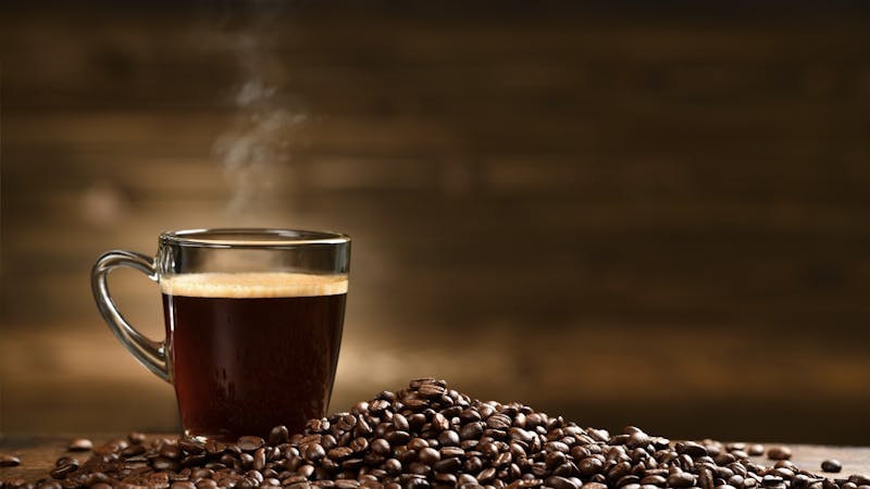 Cup glass of coffee with smoke and coffee beans on old wooden background