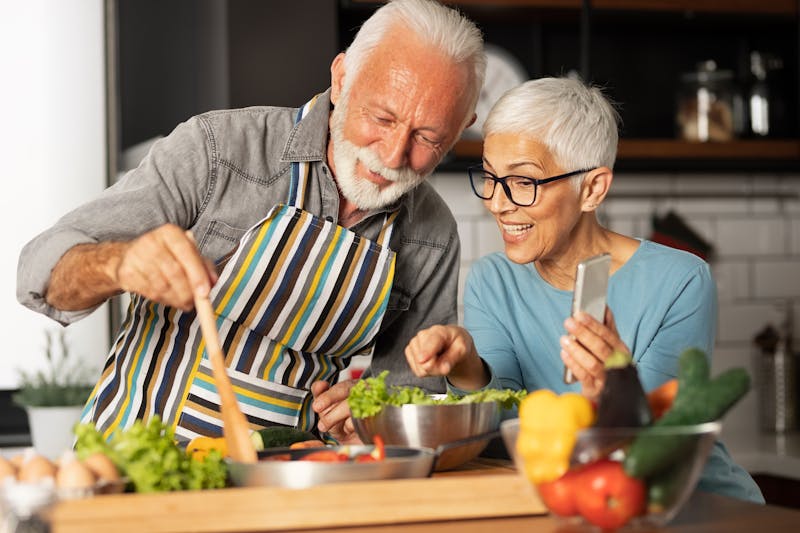 Senior couple shares a video call with their friends how prepare meal