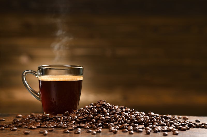 Cup glass of coffee with smoke and coffee beans on old wooden background