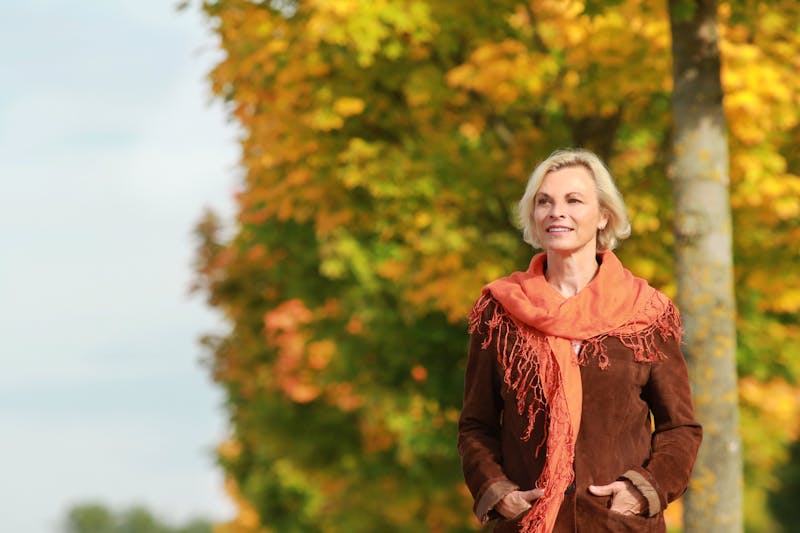 Happy mature woman walks in front of golden autumn leaves